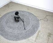 A Large Inscription, A Great Noisen2019. Solo exhibition. Optica Centre d&#39;art contemporain, Montreal QC Canada.nMixed media (Microphones, mic stand, amplifiers, gravel, cement, cable, steel, motor, electronics.)nnThe philosopher Edmund Husserl spoke of two basic modalities of time, fixed and flowing, and turned to melody to illustrate their knitting-together. For him, the experience of unified time involved retaining the immediately preceding—what just happened—in such a way as to anticipate